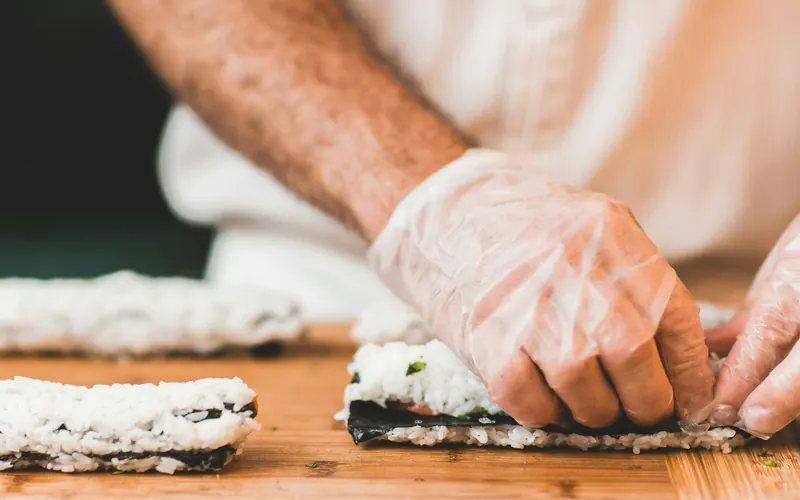 A chef's gloved hands rolling sushi on a wooden board