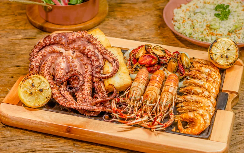 Grilled octopus, prawns and mussels with lemon on a wooden serving board